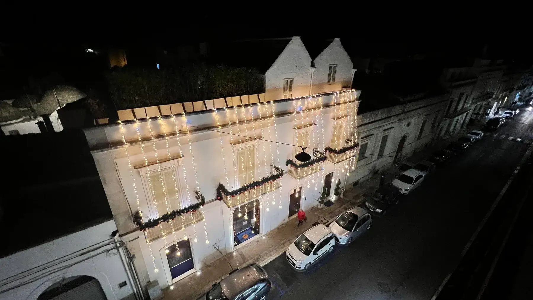Fachada do Palazzo Scotto à noite, com fios de luzes brancas e guirlandas de abeto nas sacadas. Alberobello.