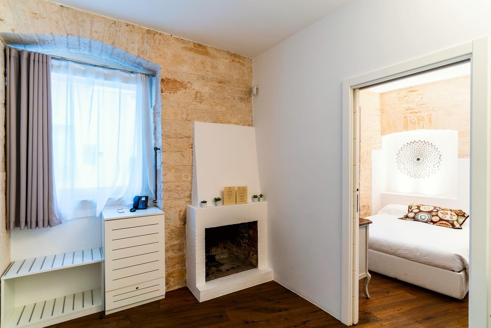 Caminetto — der weiße dekorative Kamin neben dem Fenster, und hinter der Schiebetür das Bett
