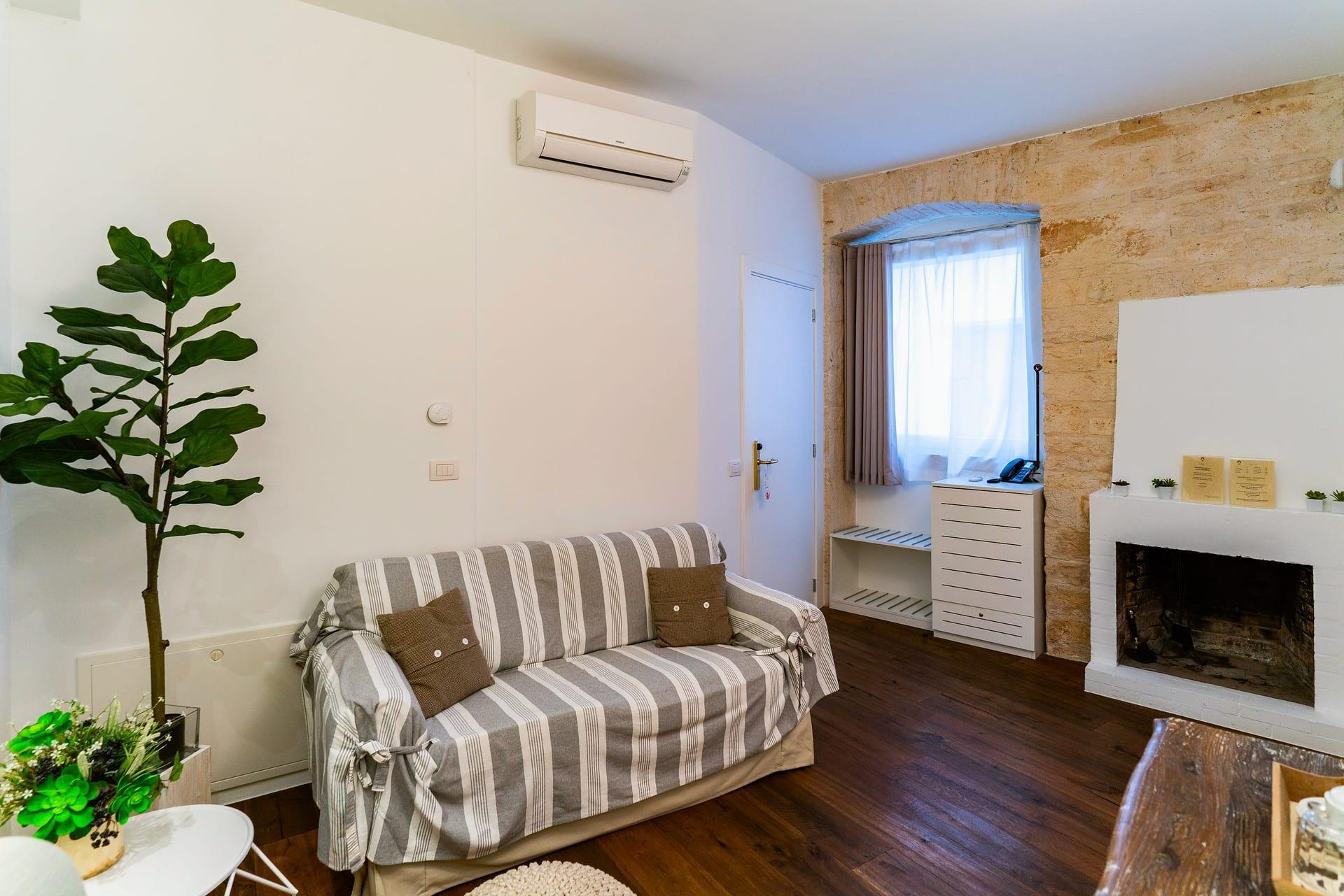 Caminetto — das grau gestreifte Sofa mit braunen Kissen, rechts der dekorative Kamin