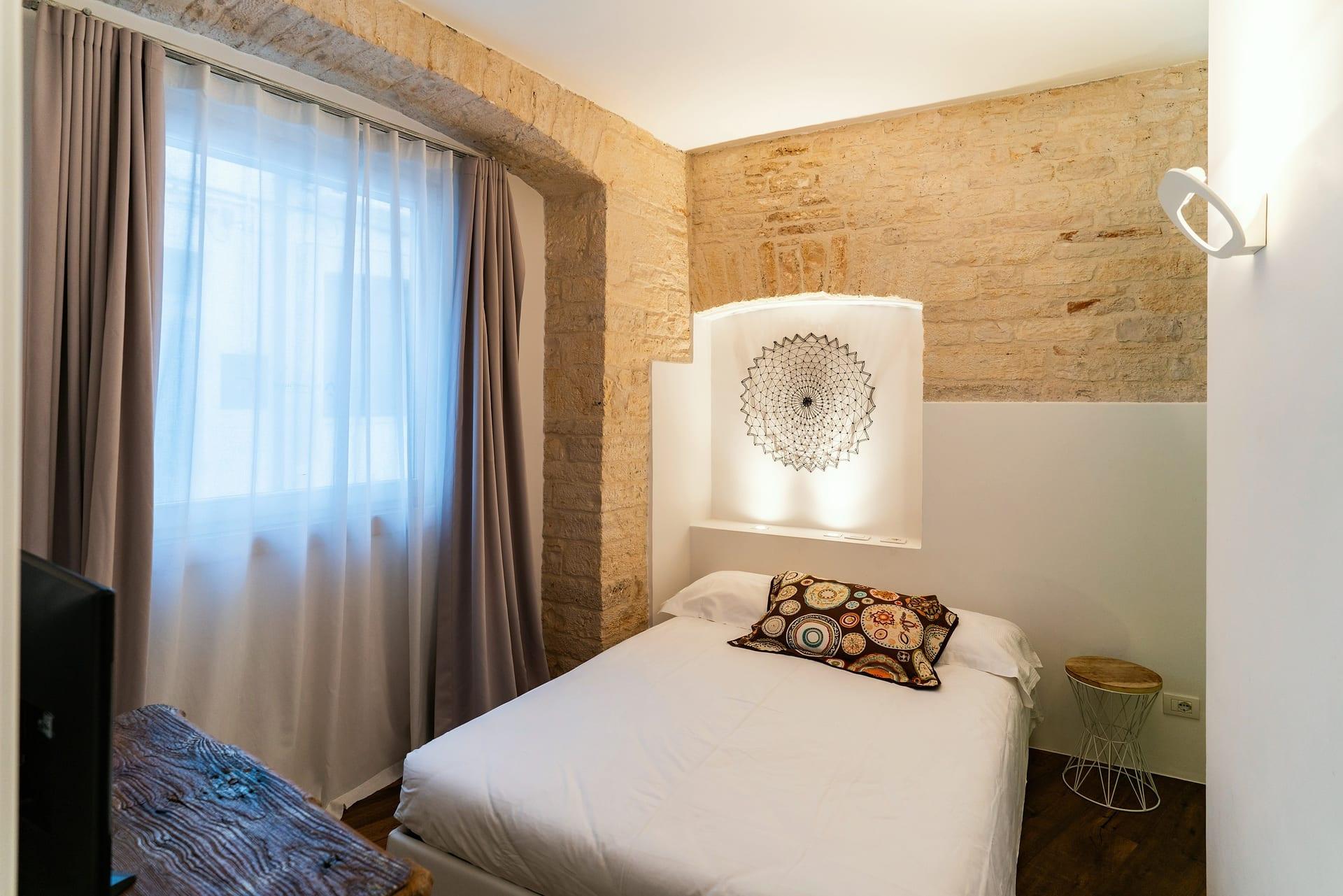Caminetto — das Bett mit dem Kissen mit bunten Kreisen, neben dem Fenster mit grauen Vorhängen