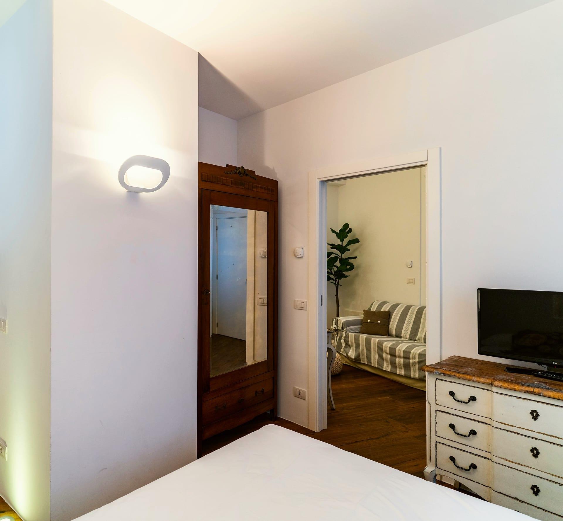 Caminetto — der Holzschrank mit Spiegel und die weiße Kommode, hinter der Tür der Wohnraum