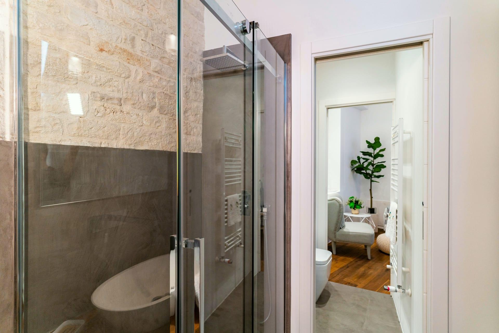 Caminetto — die Dusche mit quadratischer Regenbrause und Handtuchheizkörper, hinter der Tür der Wohnraum