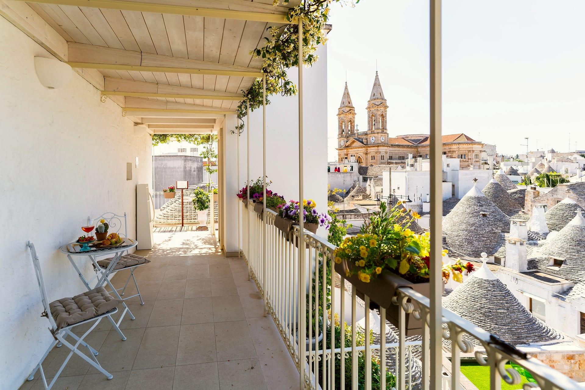 Cummerse — die Terrasse unter den Holzbalken, mit Blumenkästen am Geländer über den Trulli