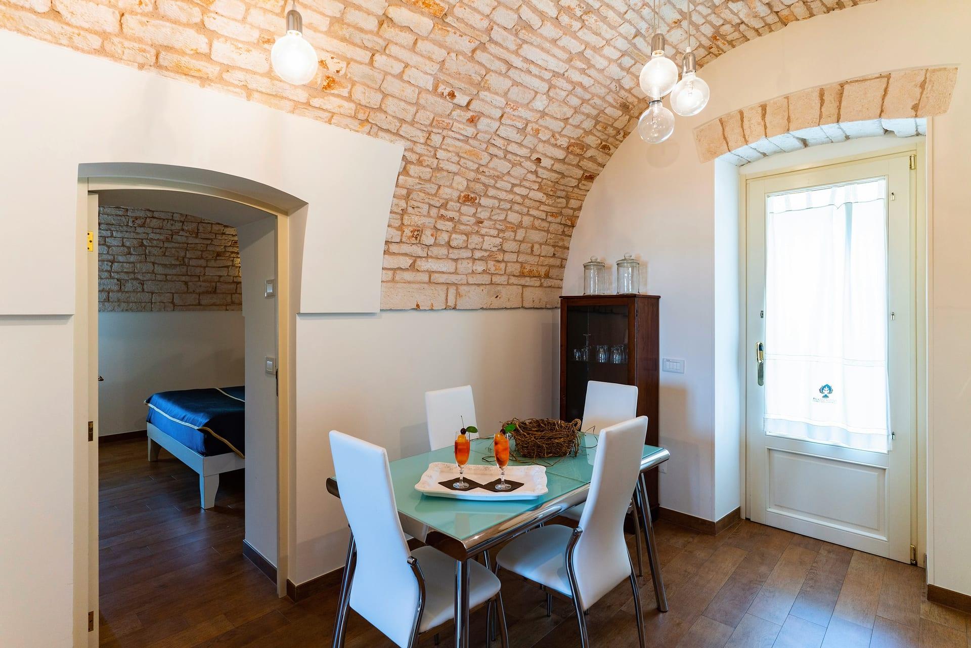 Cummerse — der Glastisch mit weißen Stühlen und das Schlafzimmer hinter dem Bogen