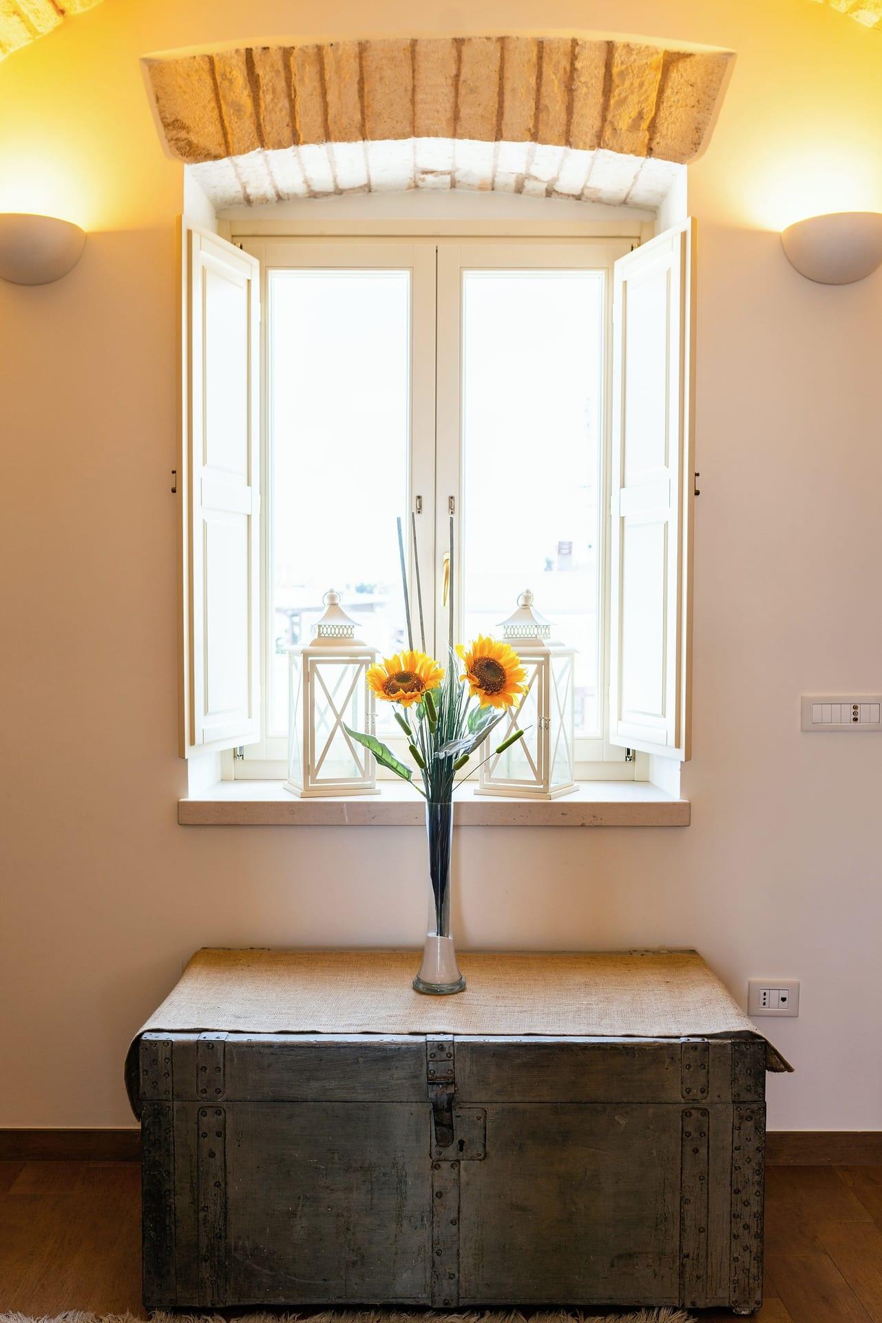 Cummerse — die Holztruhe mit Sonnenblumen, unter dem Fenster mit zwei weißen Laternen