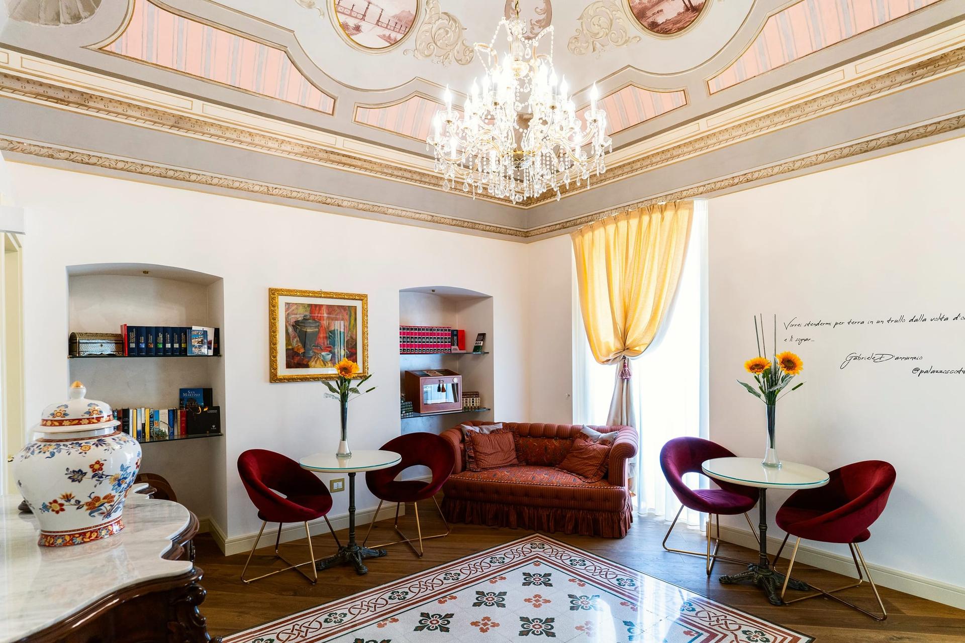 Il salone del palazzo: il soffitto dipinto, il lampadario di cristallo, il divano e le poltroncine rosse, i girasoli e il pavimento a cementine