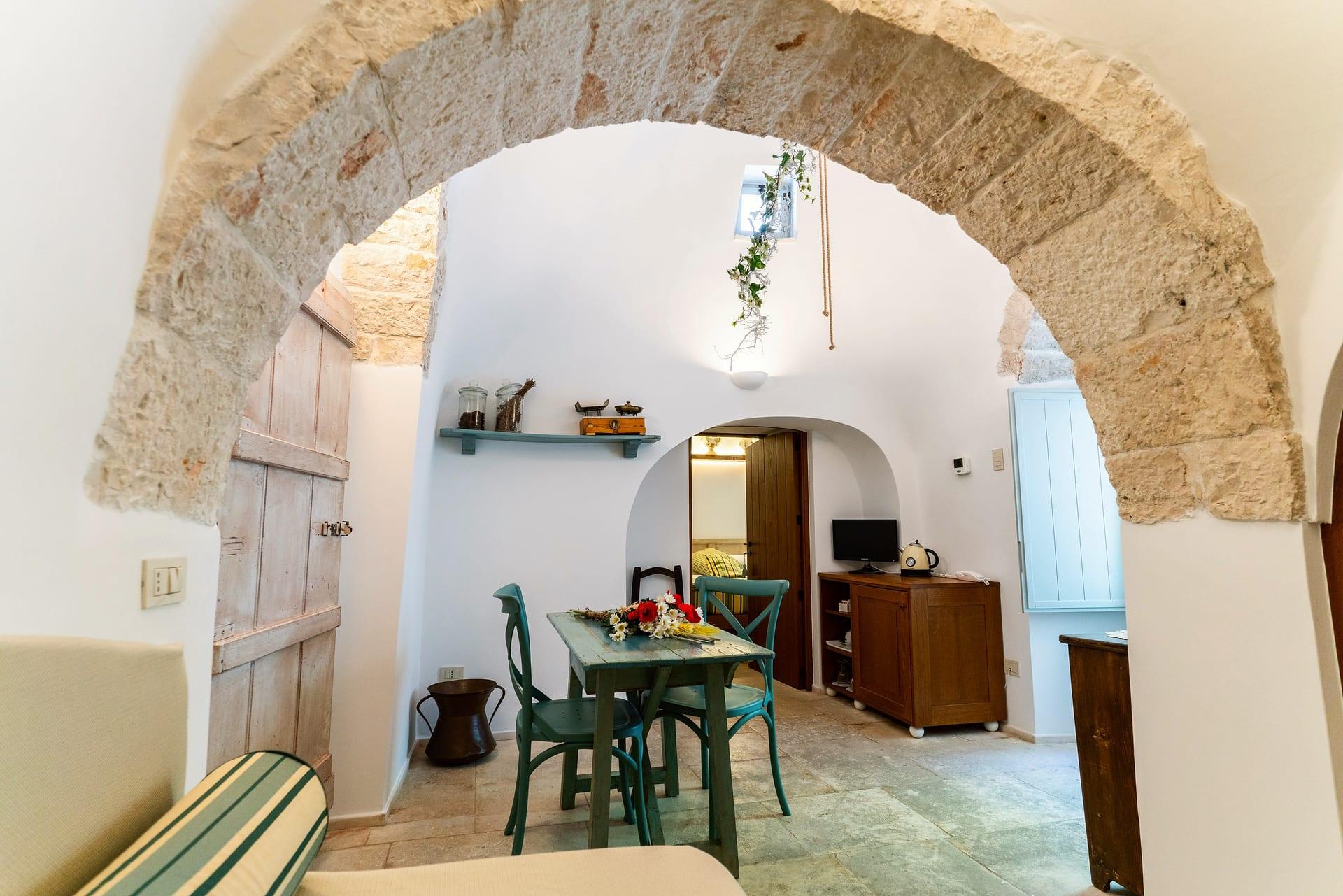 Suite Trullo — hinter dem Steinbogen der türkisgrüne Tisch und die offene Tür zum Schlafzimmer