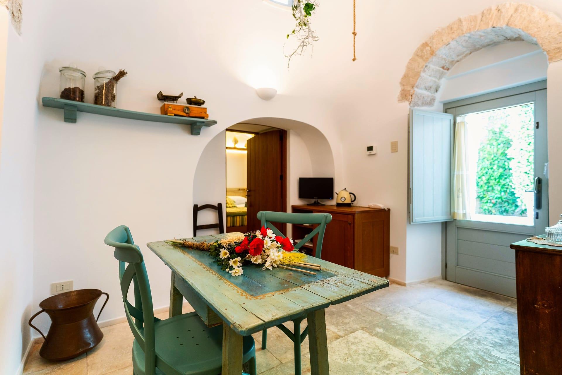 Suite Trullo — der Tisch mit roten Blumen und Margeriten, dazu die Glastür ins Grüne