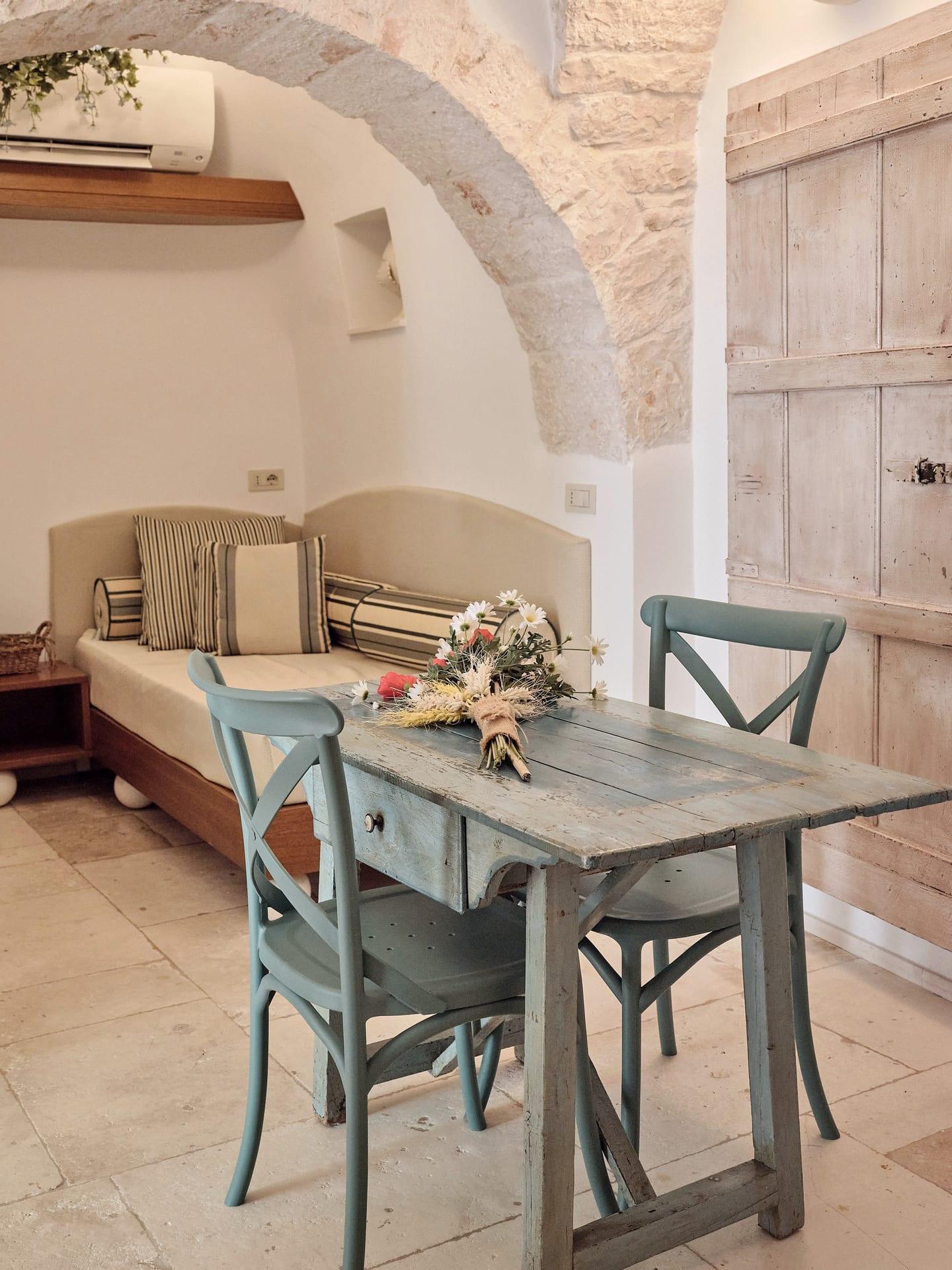 Suite Trullo — der Strauß aus Ähren und Margeriten auf dem bemalten Tisch, neben der Tür aus weiß gekalktem Holz