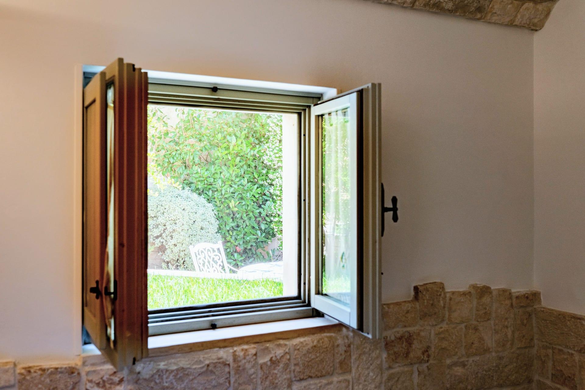 Suite Trullo — das offene Fenster zum Garten, mit Rasen und einem weißen durchbrochenen Stuhl