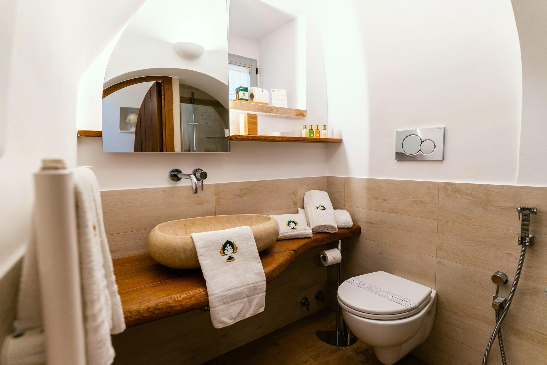 Suite Trullo — das Aufsatzwaschbecken aus Stein auf der Holzplatte, mit den bestickten Handtüchern