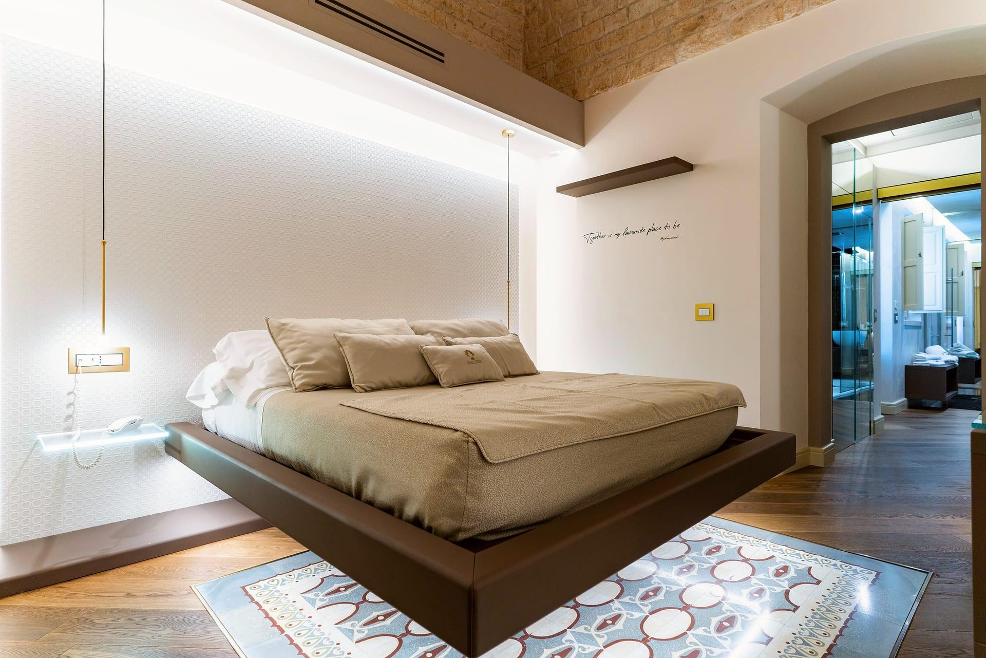 Nobile Suite — das Bett im Dreiviertelprofil, mit der dunklen Ablage und dem Schriftzug an der Wand