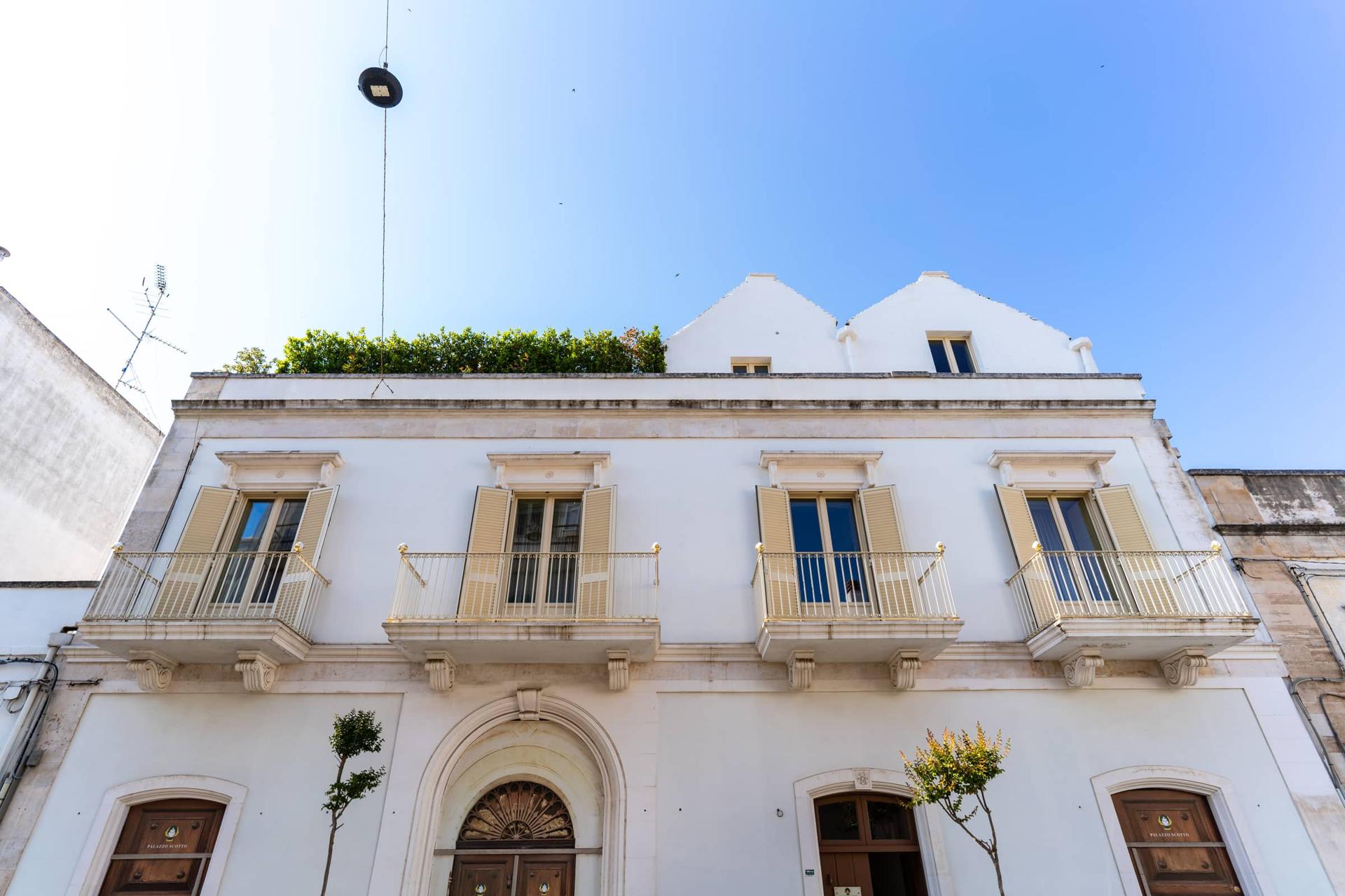 La facciata di Palazzo Scotto ad Alberobello vista di fronte, con quattro balconi, le persiane e il portone ad arco.
