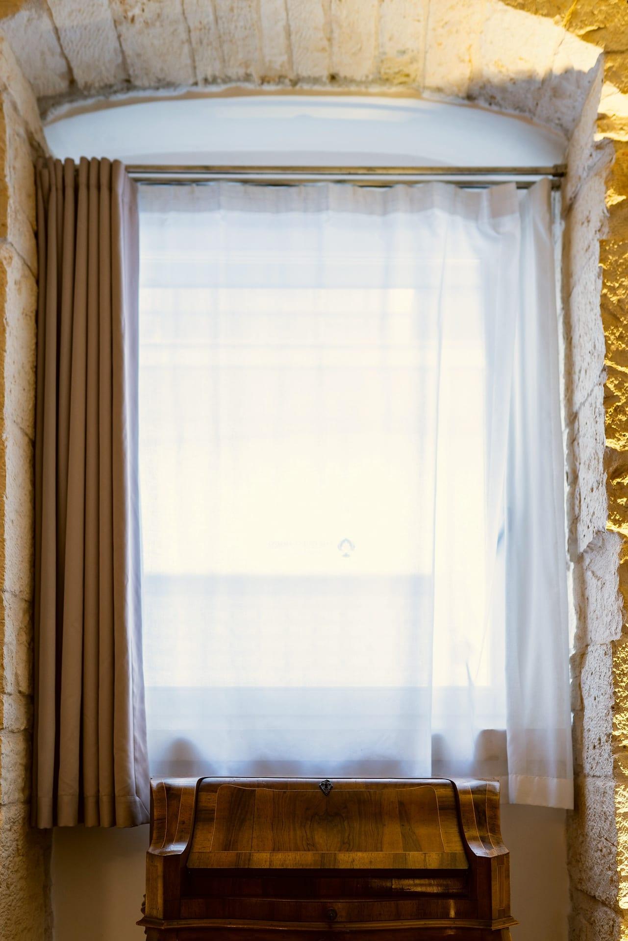 Pietra — detalle de la cortina de visillo en la ventana de arco, sobre el escritorio de madera