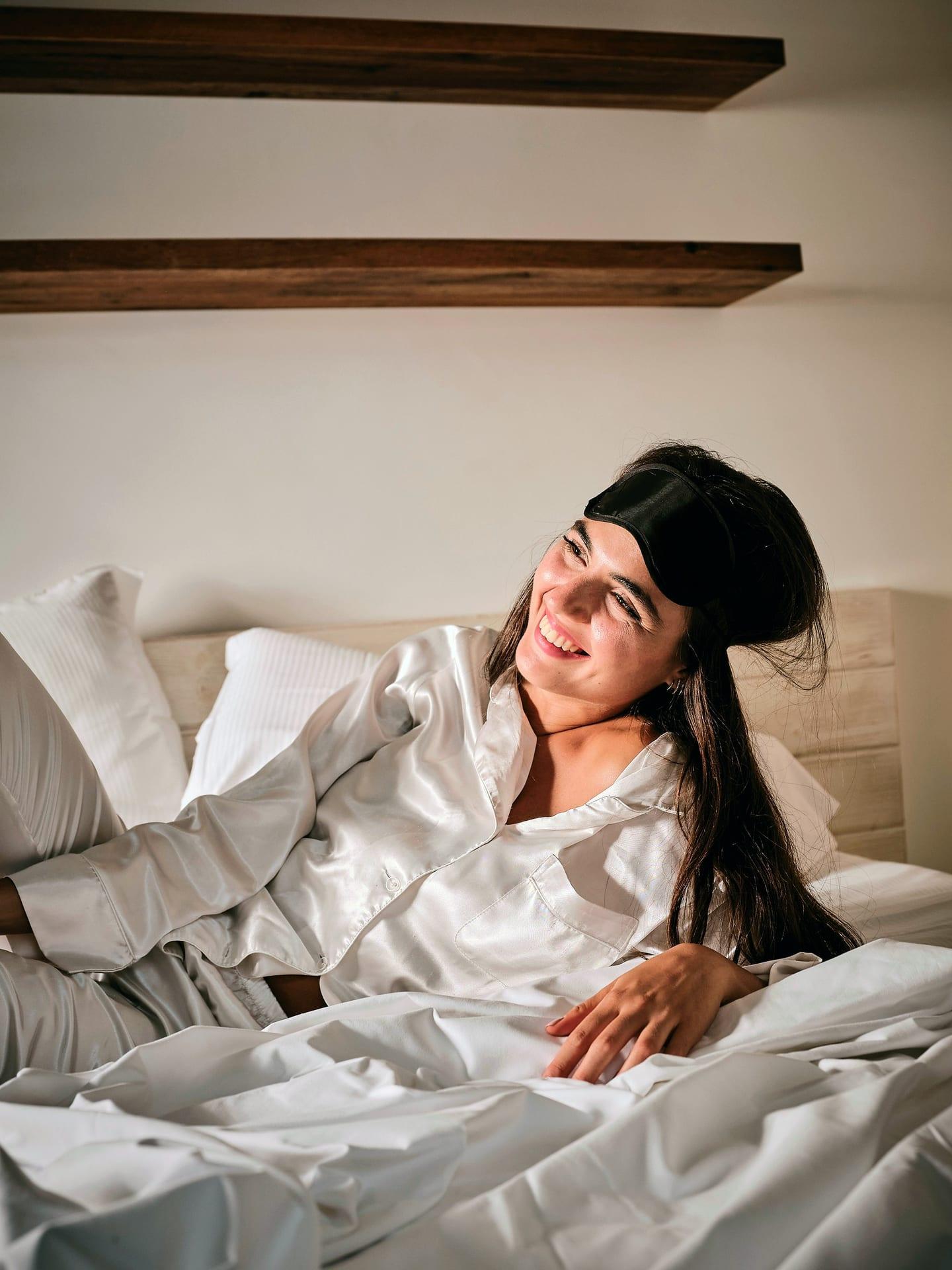 Pietra — una huésped en pijama blanco sobre la cama, con el antifaz subido a la frente