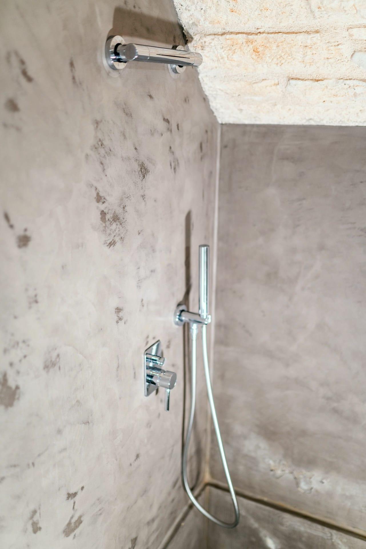 Pietra — la ducha de mano cromada y el mezclador en la pared gris, bajo la piedra vista