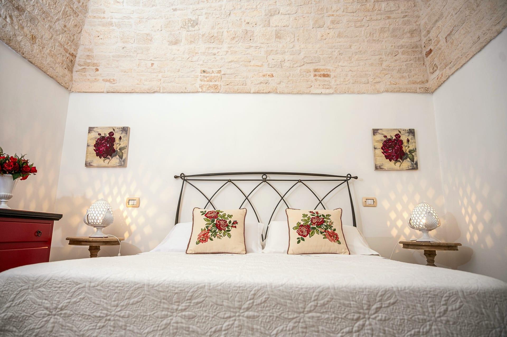 Trullo Maestro — das schmiedeeiserne Bett mit Rosenkissen, unter der Steindecke