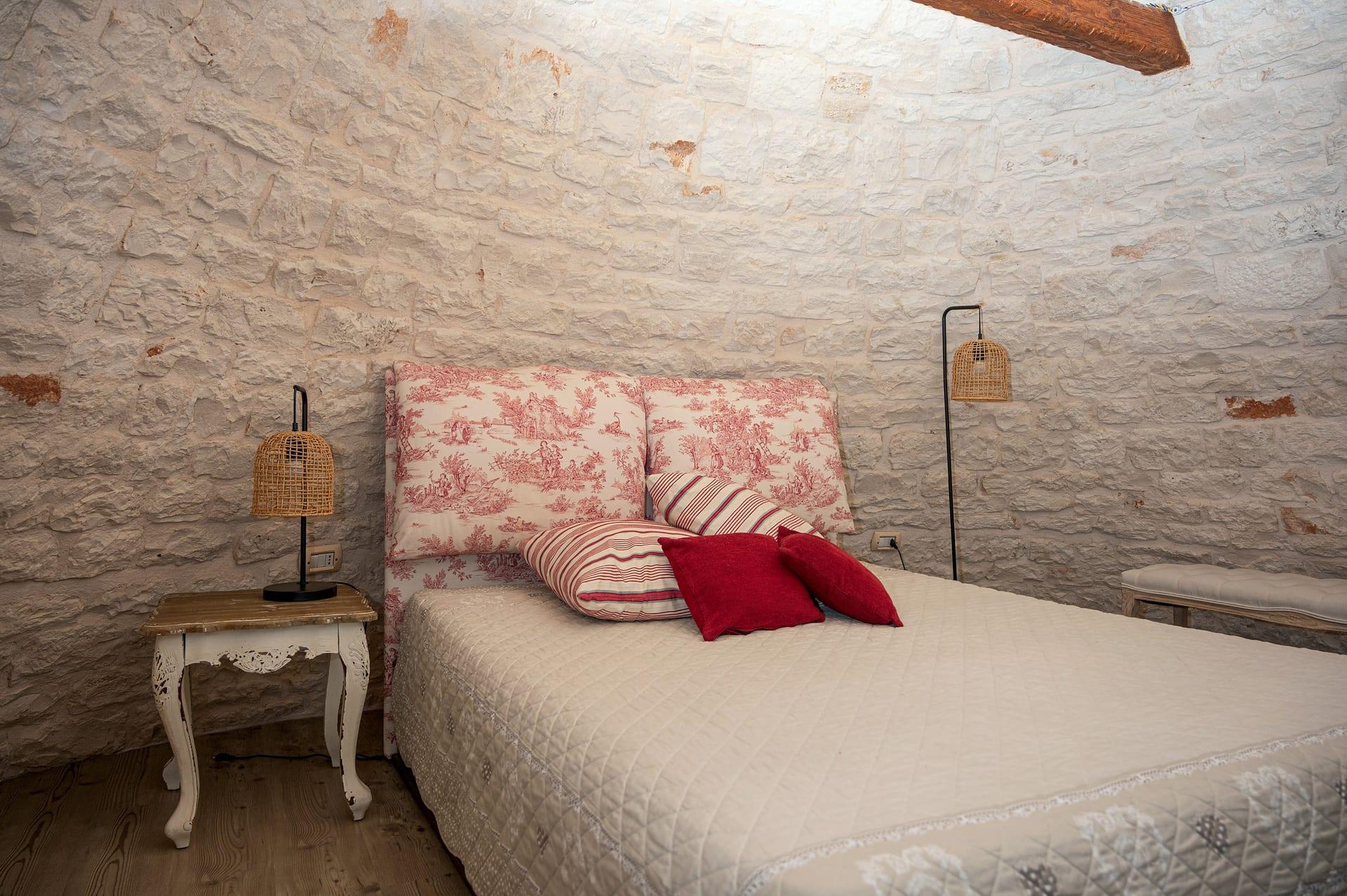 Trullo Maestro — das Bett mit roten und gestreiften Kissen, zwischen den zwei Korblampen