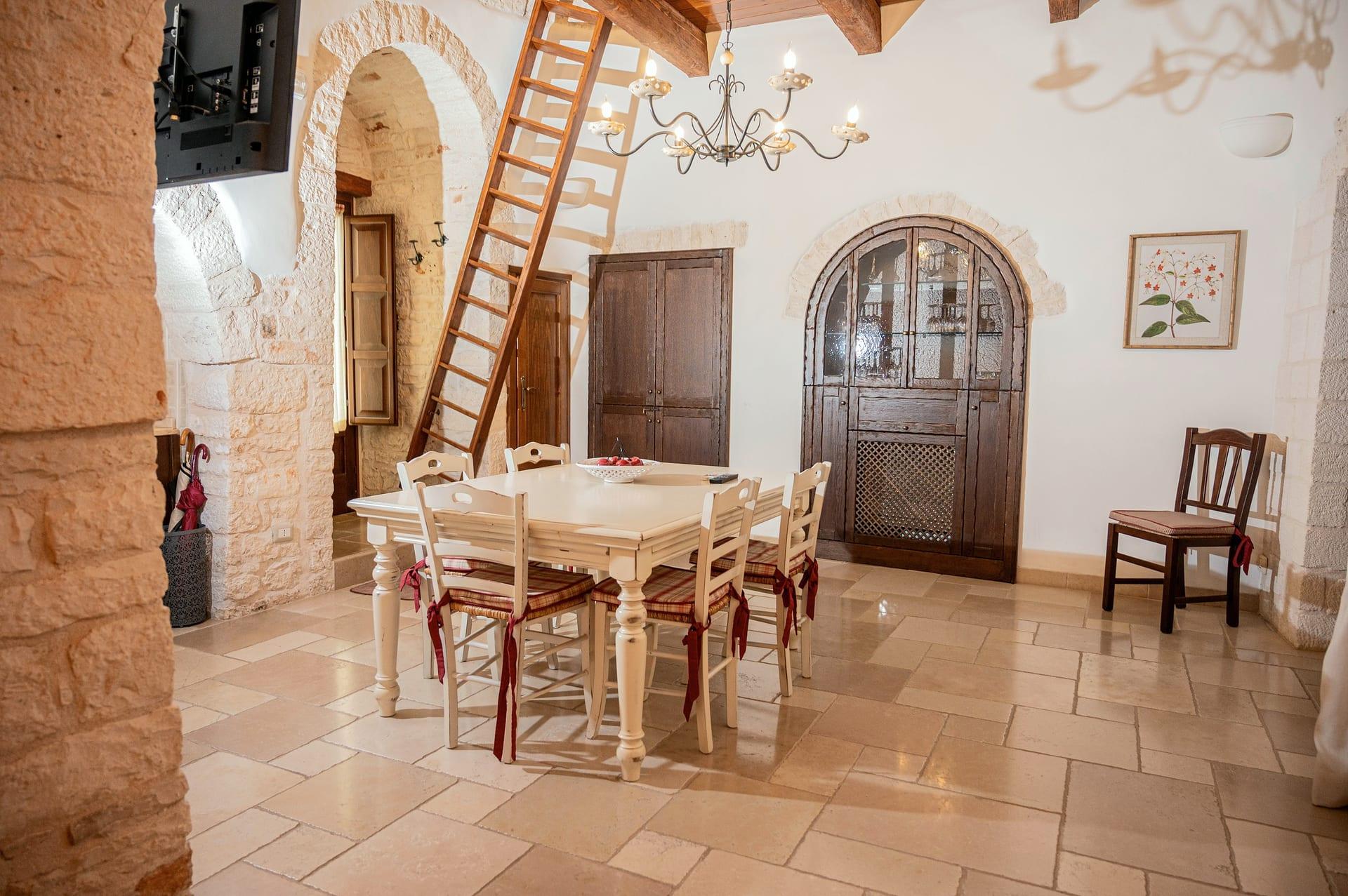Trullo Maestro — die hölzerne Bogenvitrine und der Tisch mit karierten Sitzkissen