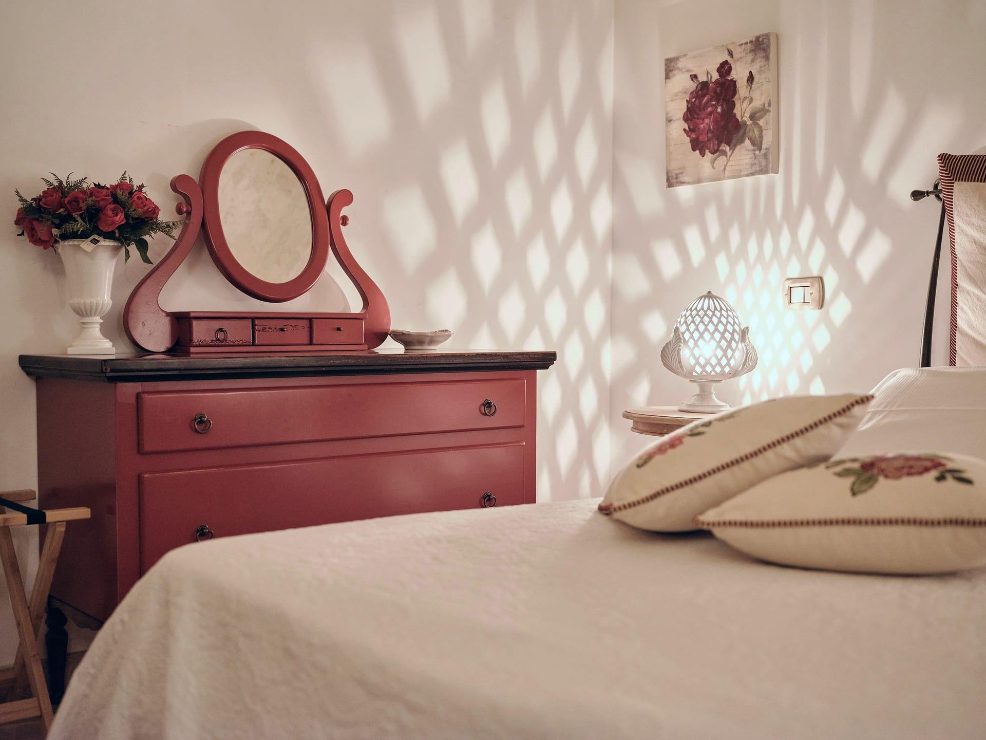 Trullo Maestro — die durchbrochene Lampe in Form eines Pumo, neben der roten Kommode mit Rosen