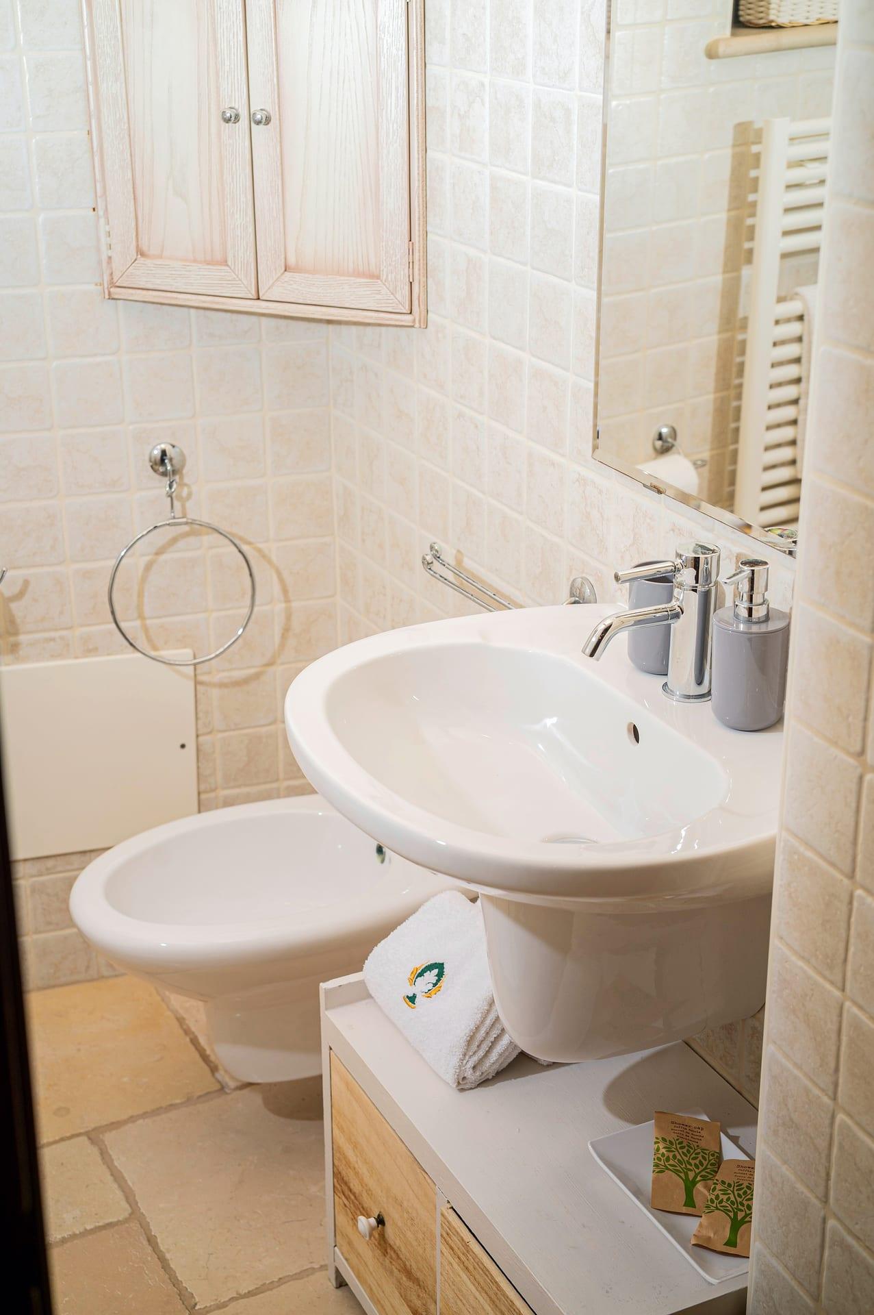 Trullo Maestro — Waschbecken und Bidet, mit dem bestickten Handtuch und den Tütchen auf dem Schränkchen