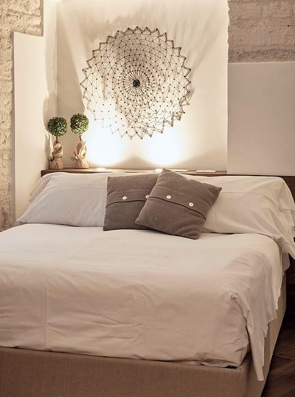 Caminetto — das Bett mit taupefarbenen Kissen unter dem Wanddeckchen