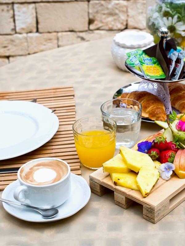 Frühstück vor der Steinmauer: Cappuccino, frisch gepresster Orangensaft, Obst auf einer kleinen Holzpalette und Cornetti auf der Etagere