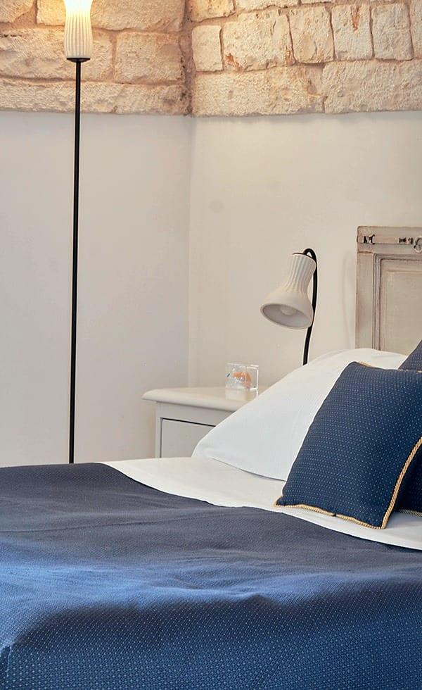 Cummerse — das Bett mit blauer Tagesdecke unter der Natursteinwand
