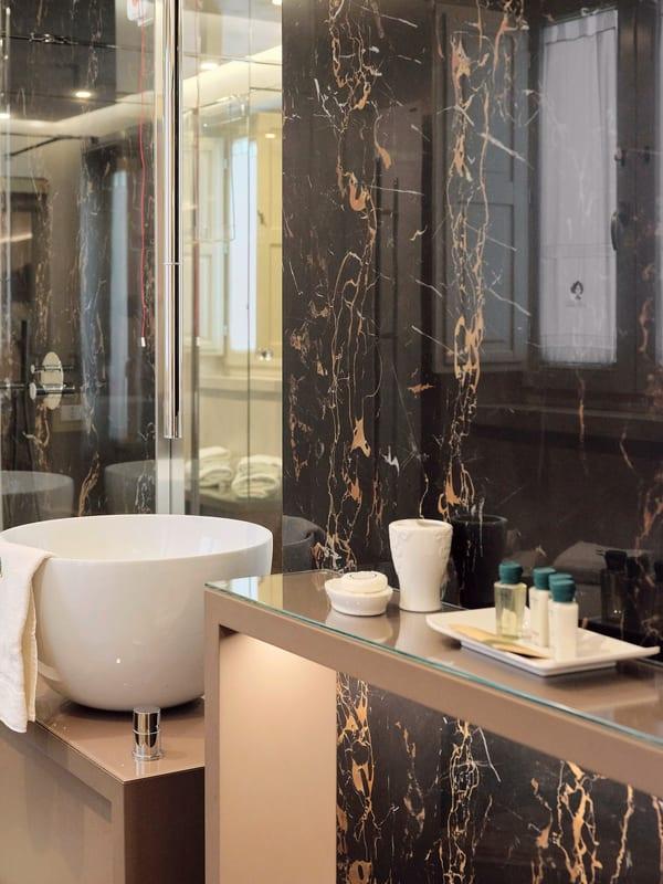 Nobile Suite — das Bad in schwarzem Marmor und Gold, mit offener Dusche