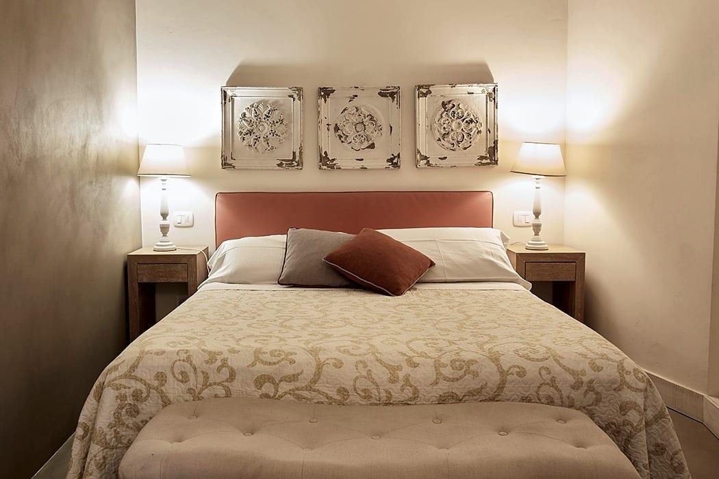 La Piccola — das Bett zwischen den beiden Nachttischlampen, mit den Zierpaneelen an der Wand
