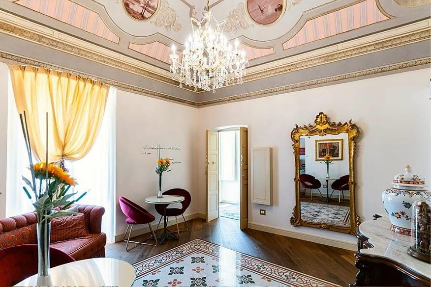 Der Salon des Palazzo: die bemalte Decke, der Kristallleuchter, der vergoldete Spiegel und das rote Sofa