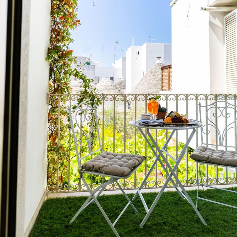 Sunny balcony with table, chairs, drinks, overlooking trulli.