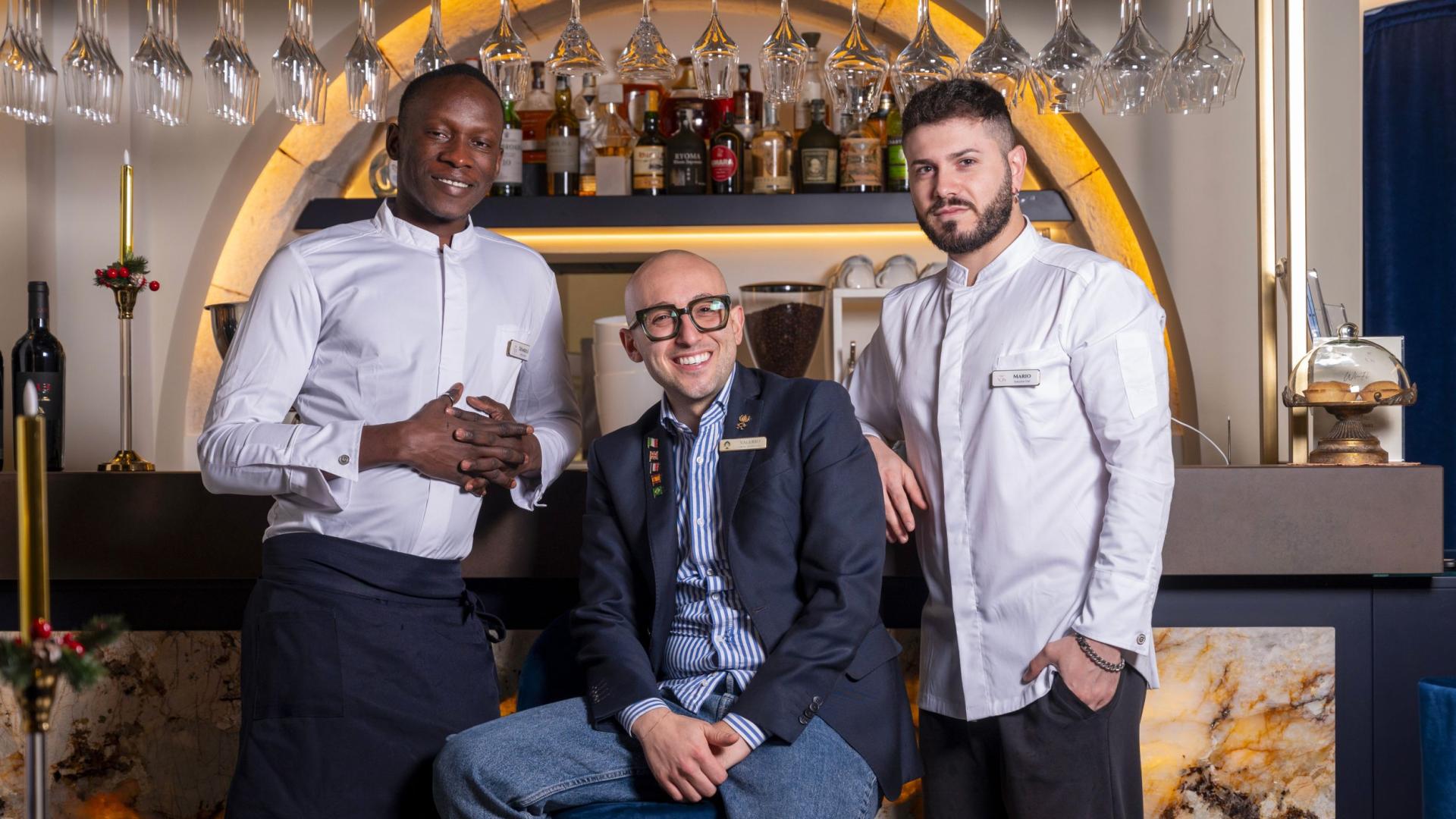 Three smiling men pose in front of an elegant bar counter.