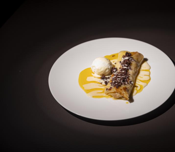Dessert with crepe, ice cream, and sweet sauce on a white plate.