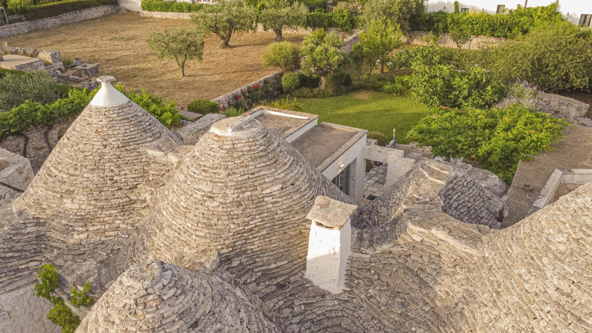 Aerial view of traditional trulli with surrounding green garden.