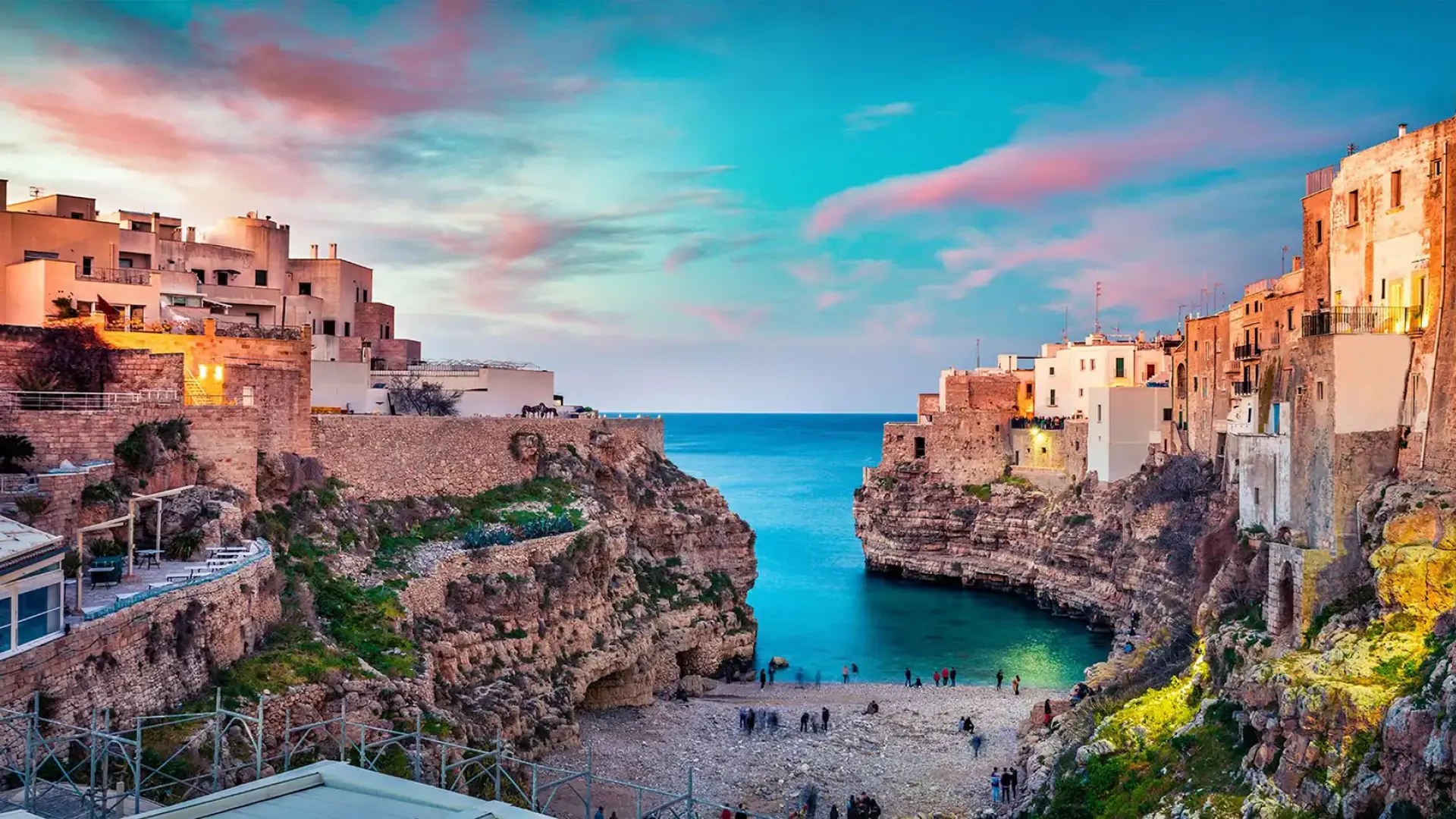Paesaggio costiero con scogliere, edifici storici e mare al tramonto.