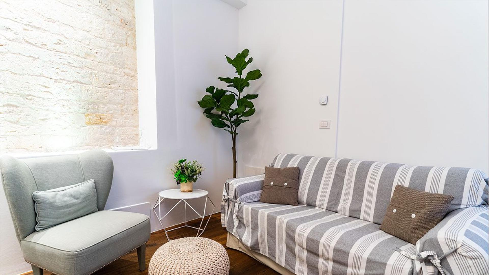 Salotto accogliente con poltrona, divano, tavolino e pianta decorativa.