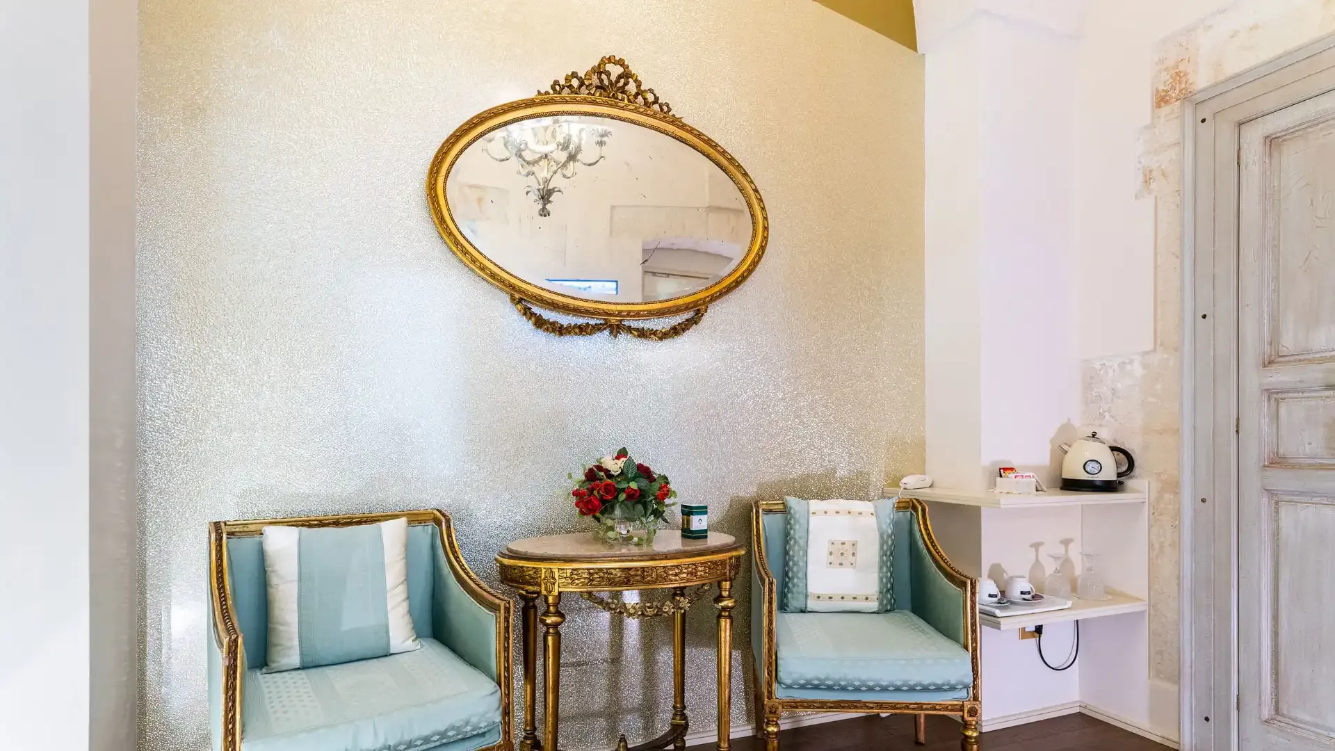 Elegant living room with vintage chairs, golden mirror, and table with flowers.