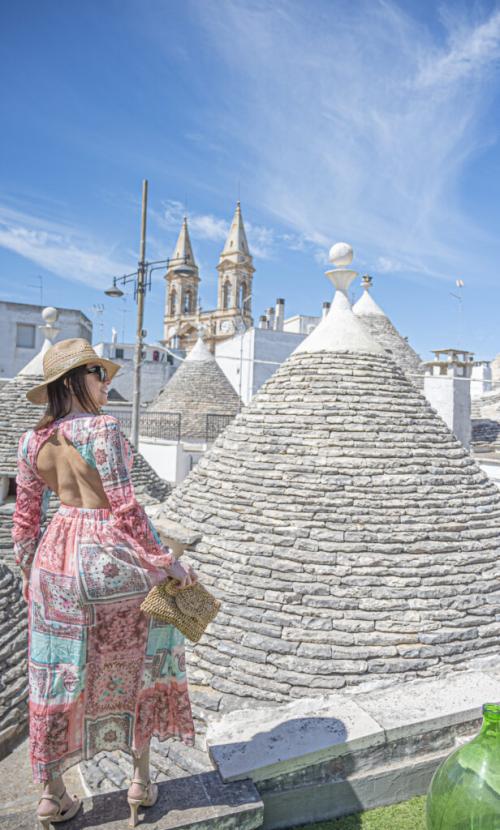 Donna con cappello ammira i trulli e il cielo azzurro.