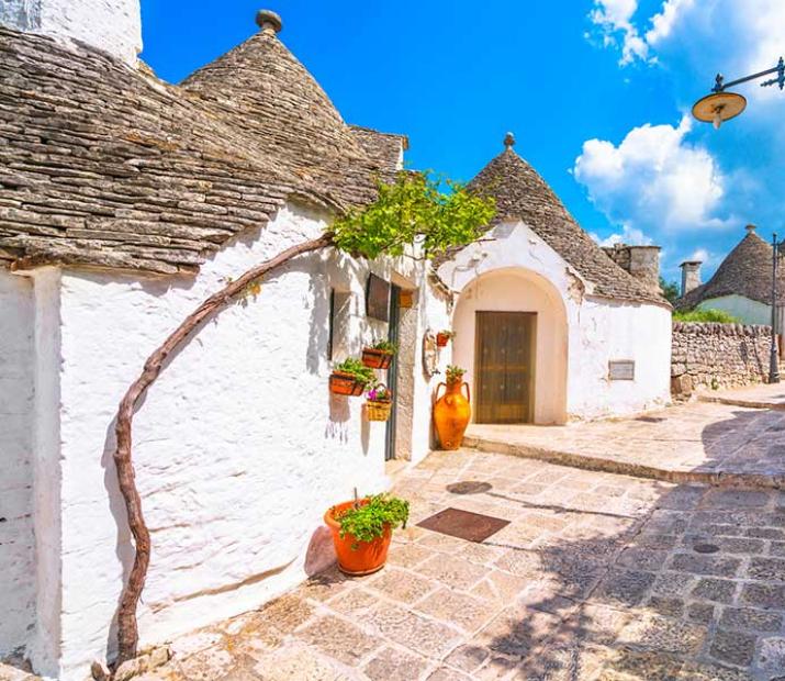 Strada pittoresca con case bianche e tetti conici, tipiche della Puglia.
