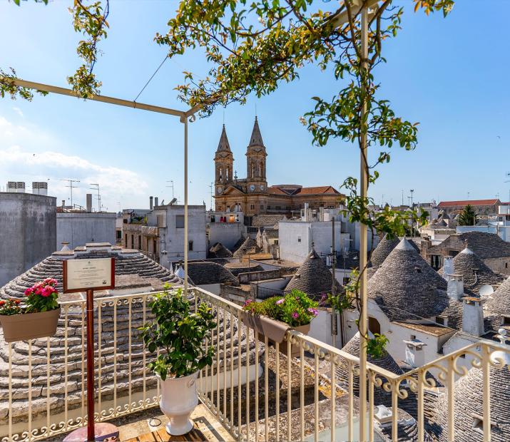 Vista dei trulli e della chiesa di Alberobello da un balcone fiorito.