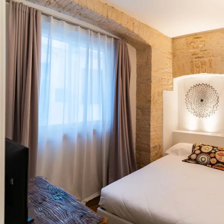 Camera accogliente con pareti in pietra, letto matrimoniale e decorazioni artistiche.