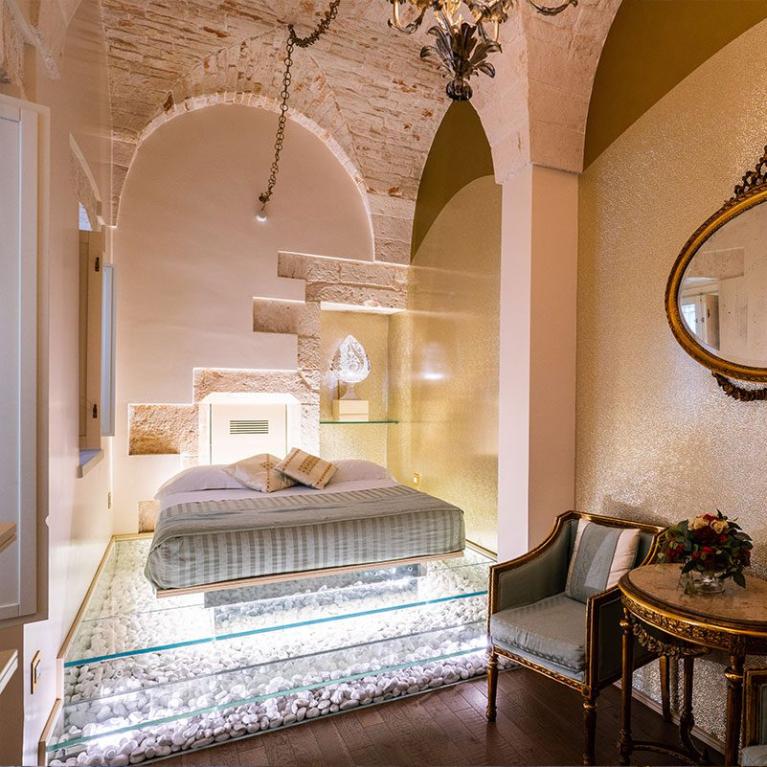 Elegant room with suspended bed on glass and antique furnishings.