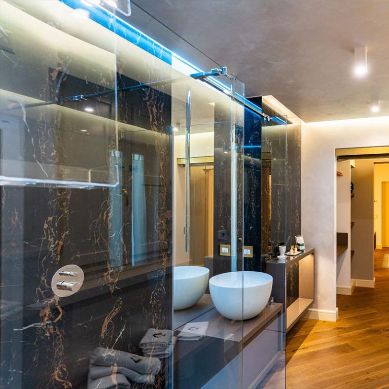 Bagno moderno con doppio lavabo, pavimento in legno e doccia in marmo.