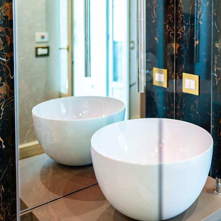 Lavabo moderno con rubinetto sospeso e pareti in marmo.
