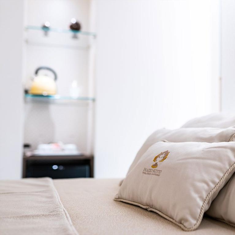 Camera elegante con cuscini su letto e scaffale con bollitore.