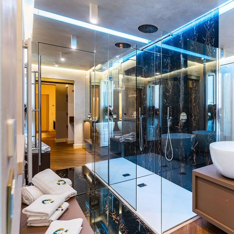 Bagno moderno con doccia in vetro, lavabi bianchi e dettagli in marmo nero.