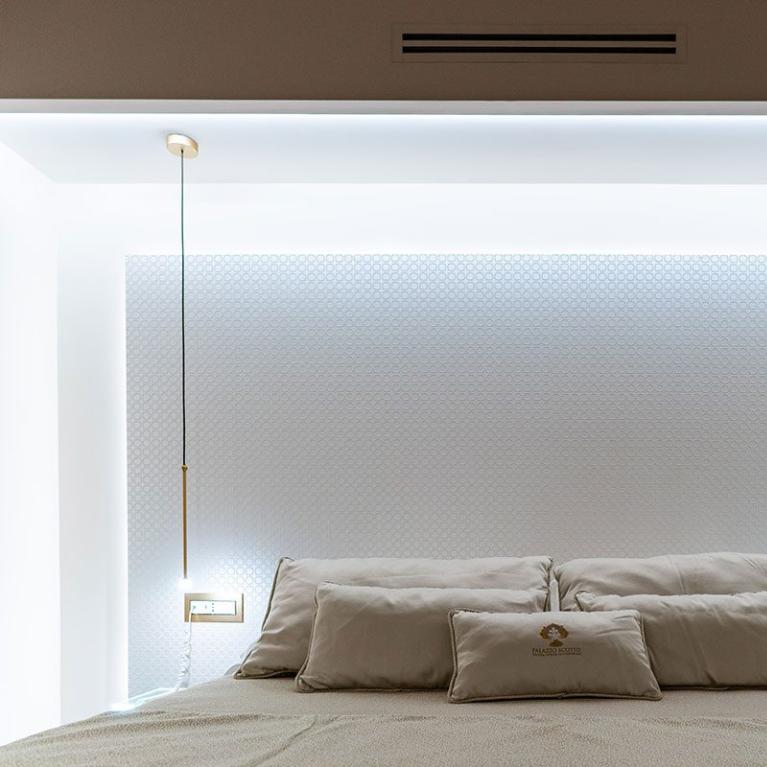 Camera da letto moderna con illuminazione a sospensione e cuscini beige.