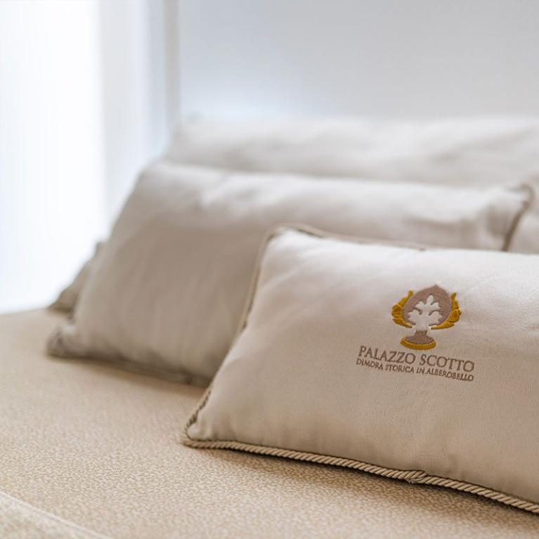 Cuscini beige con logo Palazzo Scotto, dimora storica in Alberobello.