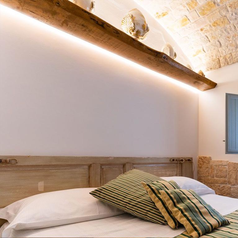 Chambre chaleureuse avec lit, coussins rayés et fenêtres avec volets.